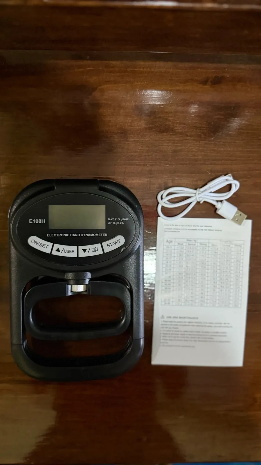 X-Grip PowerTester in the box — the digital hand dynamometer with its USB-C charging cable and grip-strength reference card
